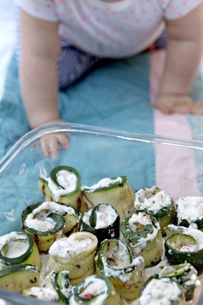 Dish of grilled zucchini rollatini in front of baby on picnic blanket