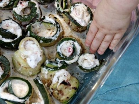 Child's hand grabbing grilled zucchini rollatini from serving dish