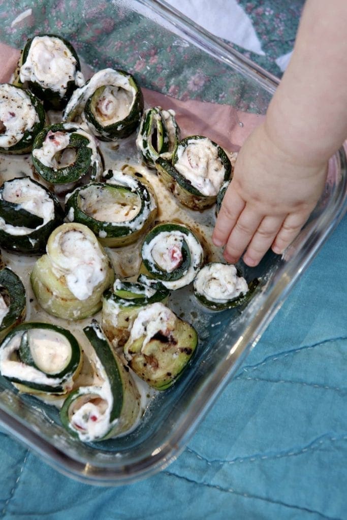 Child's hand grabbing grilled zucchini rollatini from serving dish 