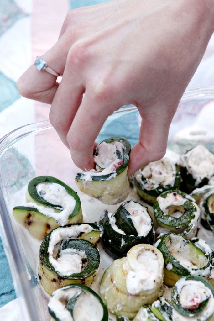 Hand picking up bite sized grilled zucchini rollatini from dish 