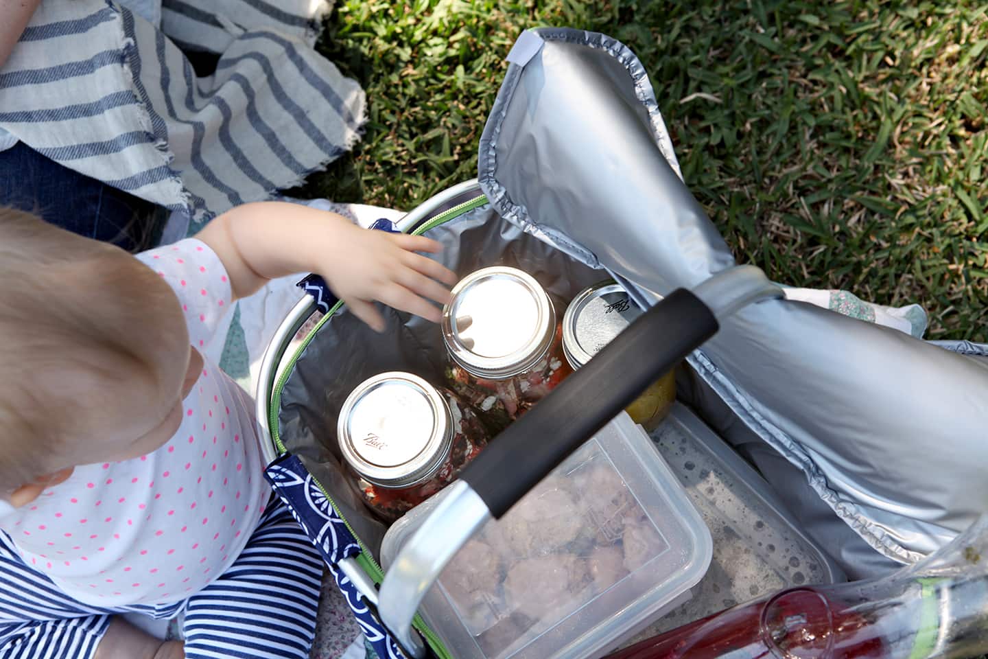 Child's hand reaching into picnic basket filled with packaged food items 