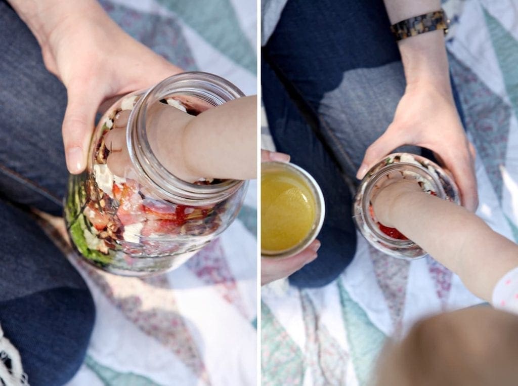 Hand holding glass jar of salad with child's hand reaching in 