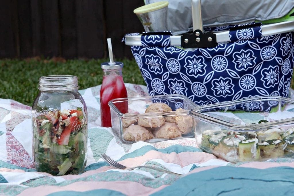 Different containers of food on a blanket with picnic basket 