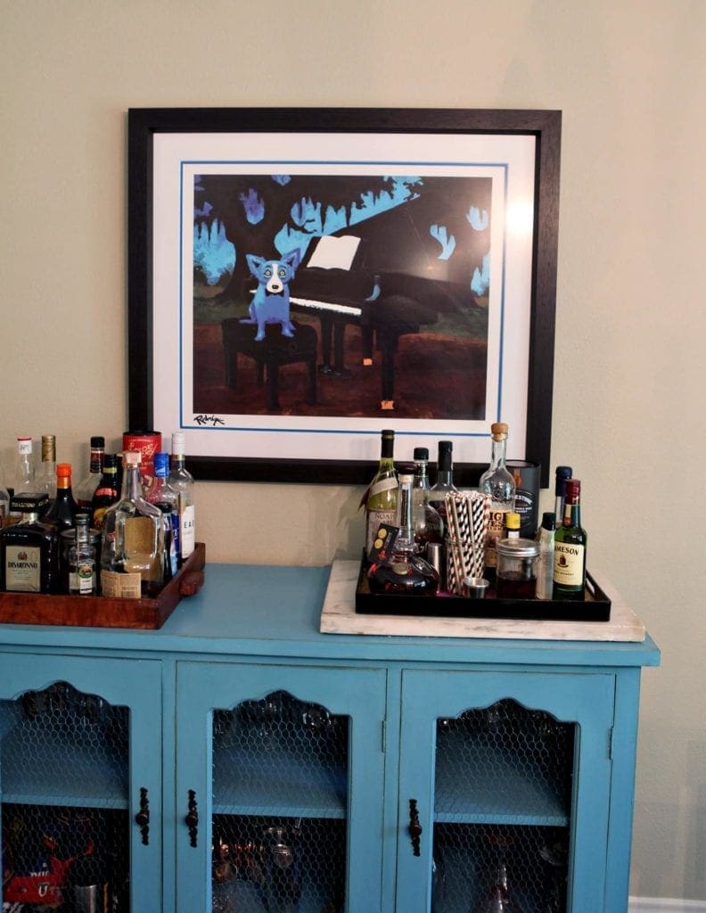 Alcoholic glass bottles on top of a cabinet in front of framed picture 