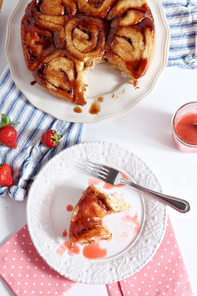 Strawberry Cinnamon Breakfast Buns, half eaten, on a white plate and a colorful white, pink and blue backdrop