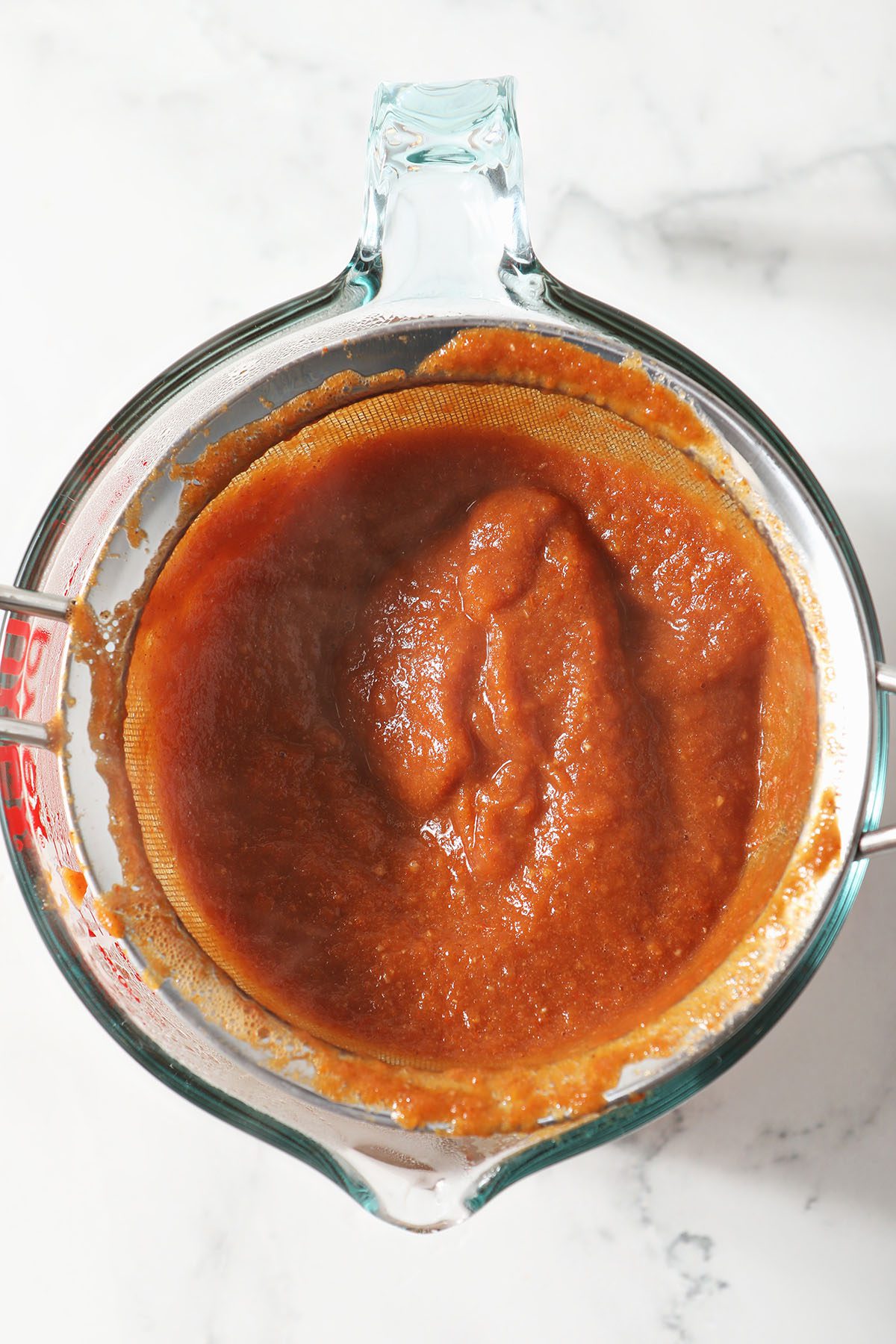 Red enchilada sauce being strained in a mesh sieve