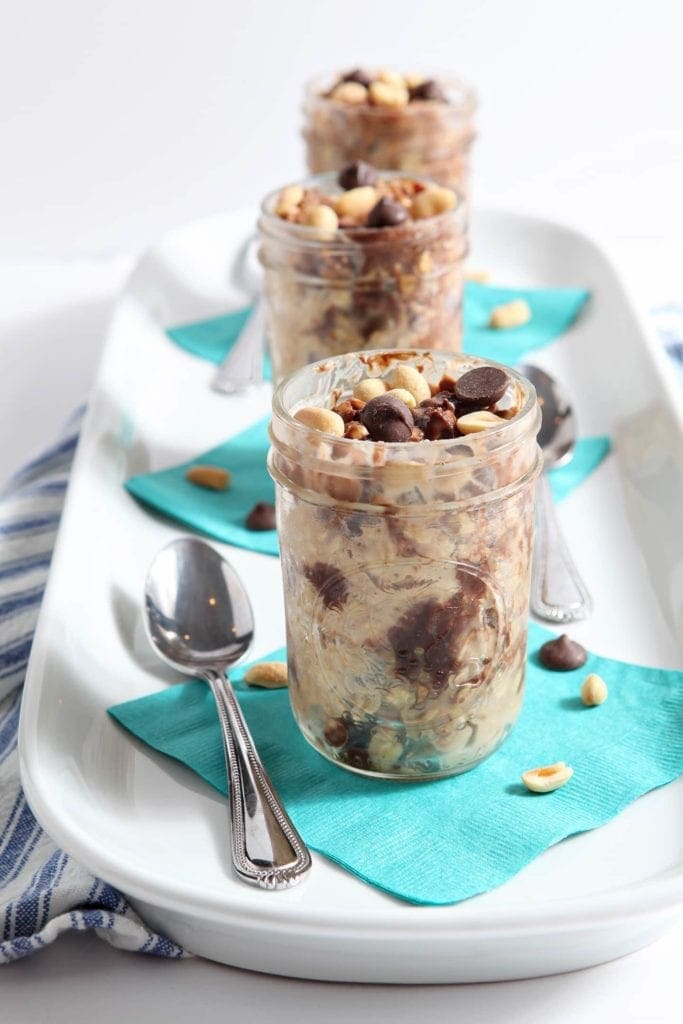 Three glass jars of Peanut Butter Chocolate Chip Overnight Oats on white serving dish 