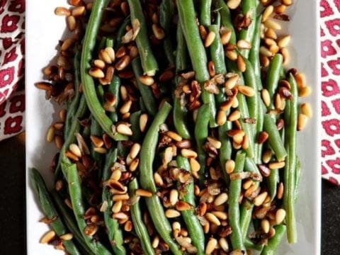 Steamed green beans with pine nuts on a white platter from above