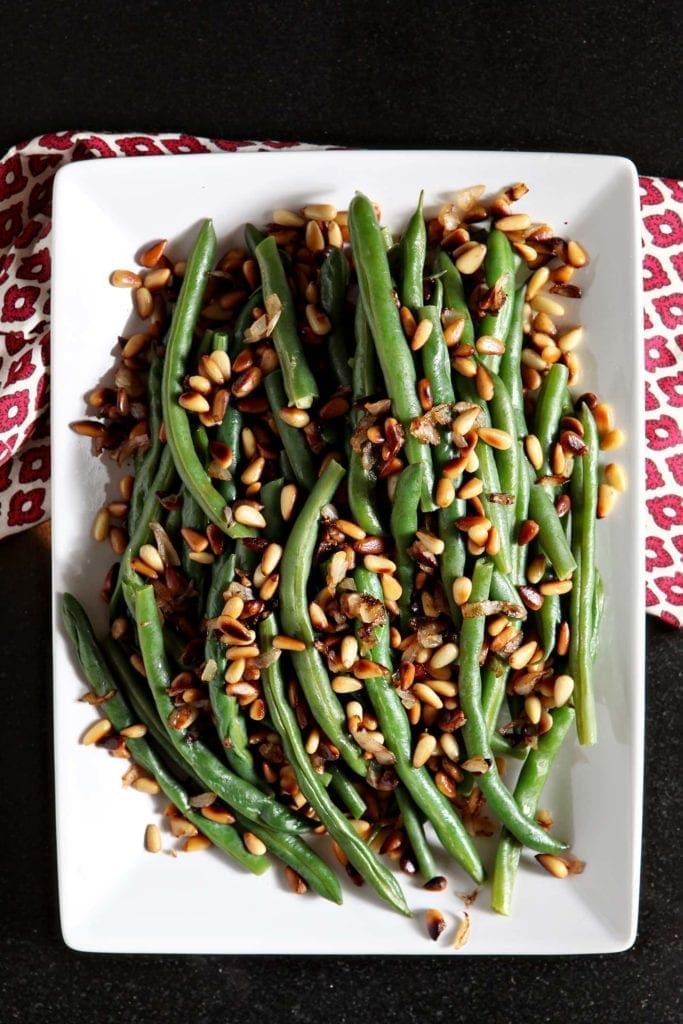 Steamed green beans with pine nuts on a white platter from above