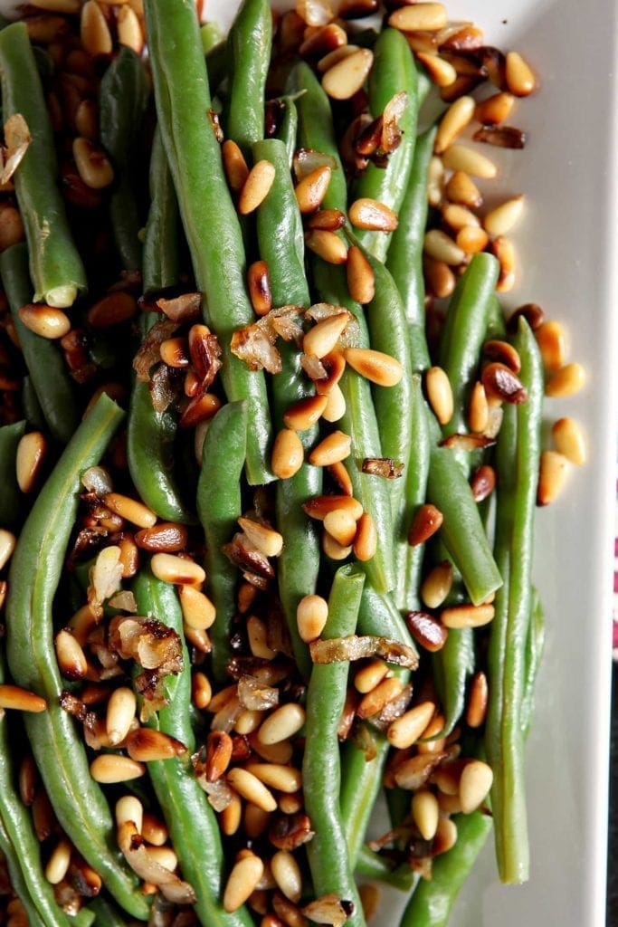 Close up of steamed green beans with pine nuts on a white platter from above