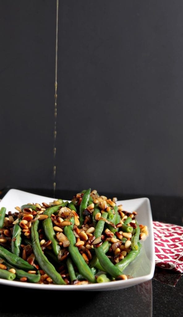 Oil drizzles down onto a platter of green beans