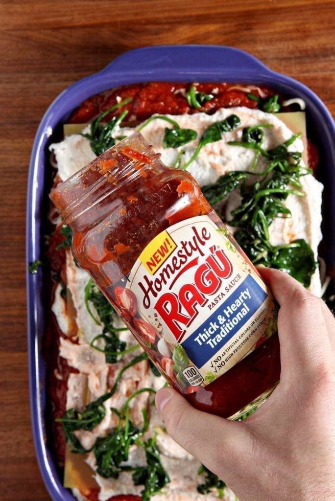 Hand holding jar of pasta sauce over vegetarian spinach lasagna