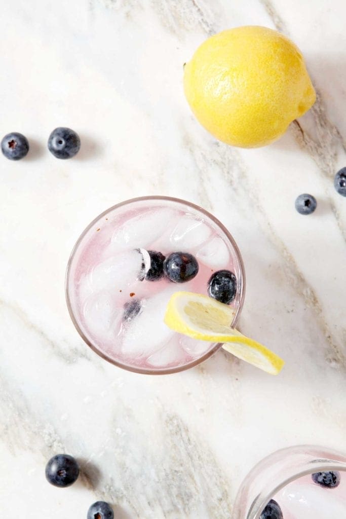 A cup with ice and pink liquid with blueberries and a lemon slice