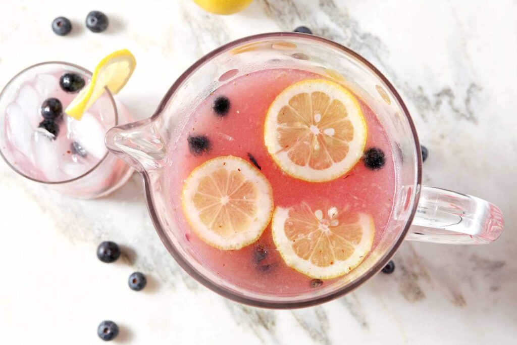 A pitcher holding purple liquid and lemon slices on marble