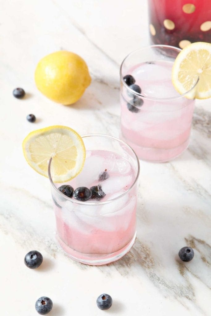 Two glasses of Blueberry Lemonade garnished with fresh blueberries and wheels of lemons