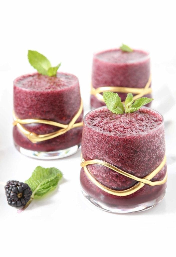 Three Blackberry Gin Slushes sit on a white serving platter with fresh blackberries and mint surrounding them.