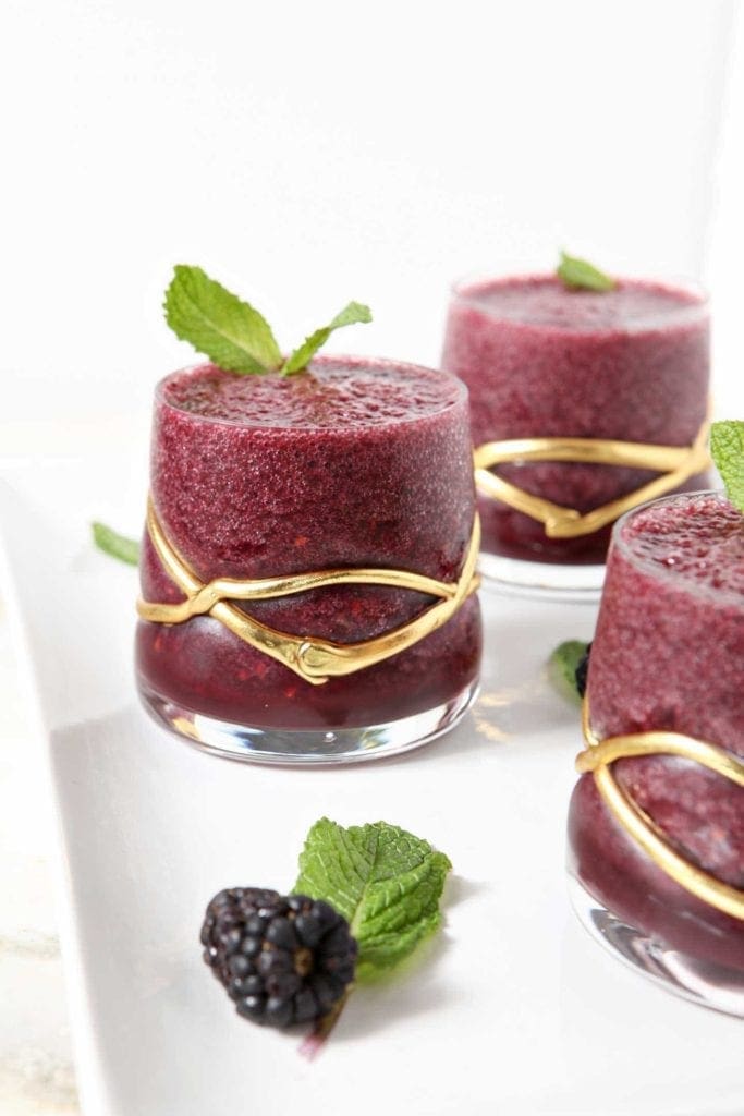 Three glasses of blackberry gin slushes with mint and berry garnish