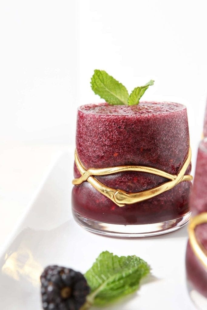 A Blackberry Gin Slush, garnished with a mint leaf, sits on a white platter.