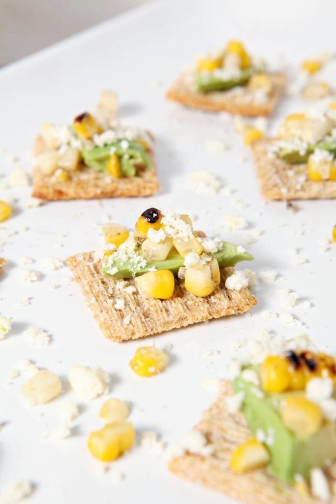 Several Cotija Corn Avocado TRISCUIT Crackers sit on a white platter before serving at a summertime gathering