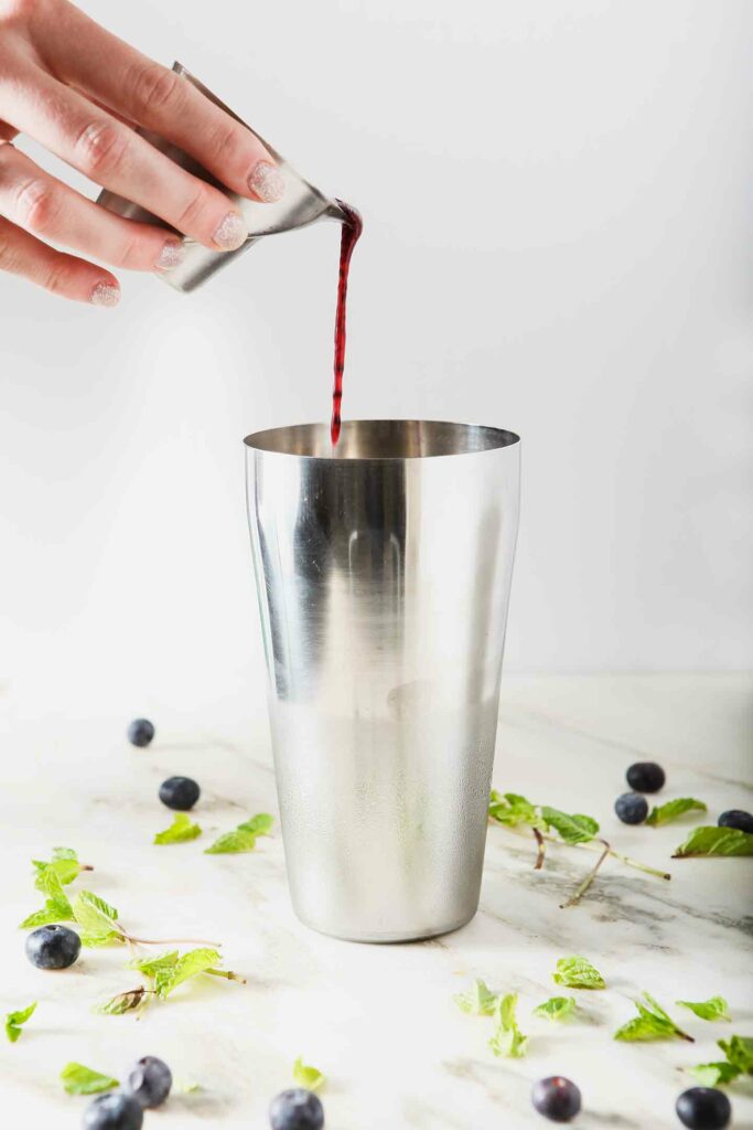 Blueberry puree pours into a metal cocktail shaker