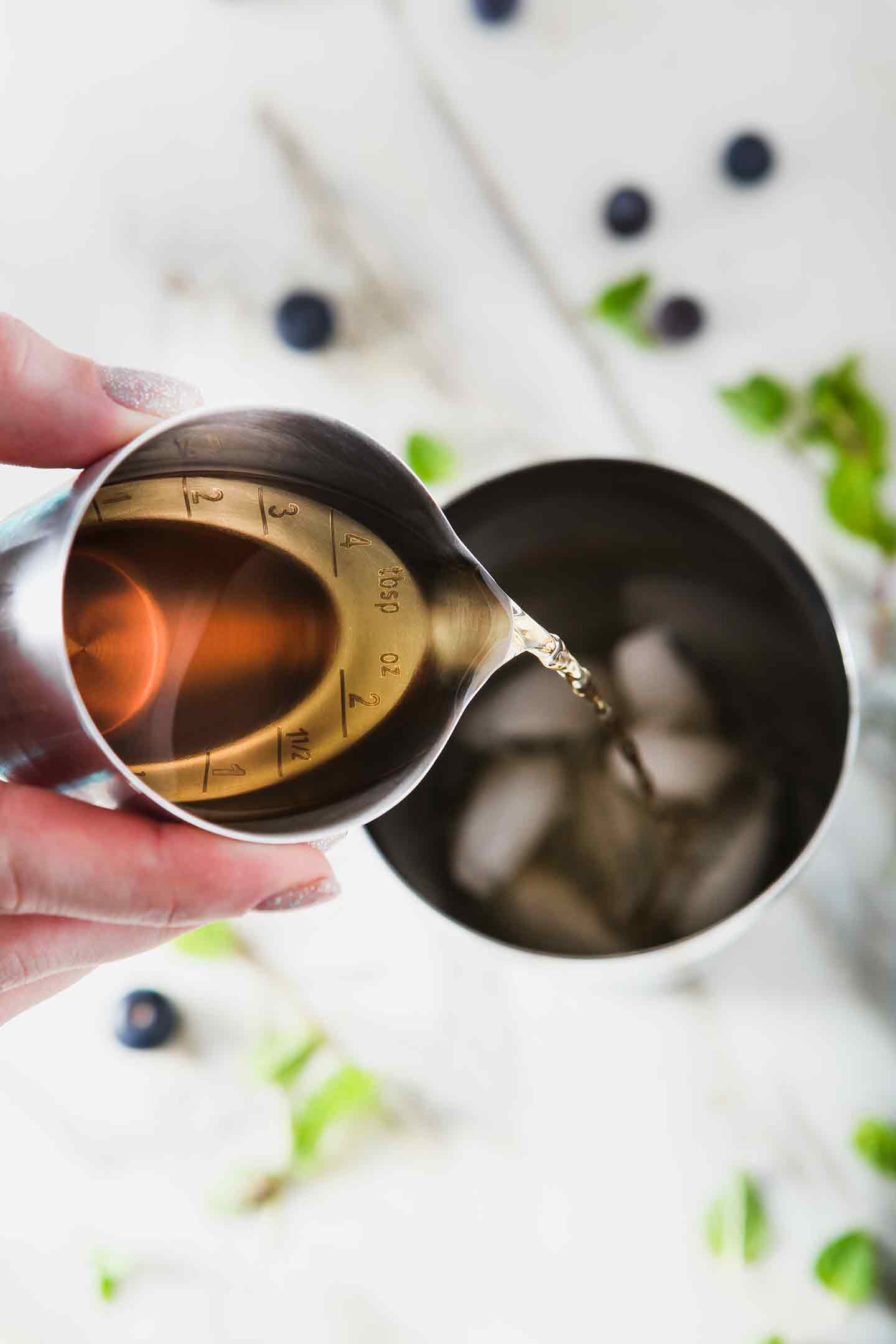 Bourbon is poured into a cocktail shaker for Blueberry Mint Juleps.