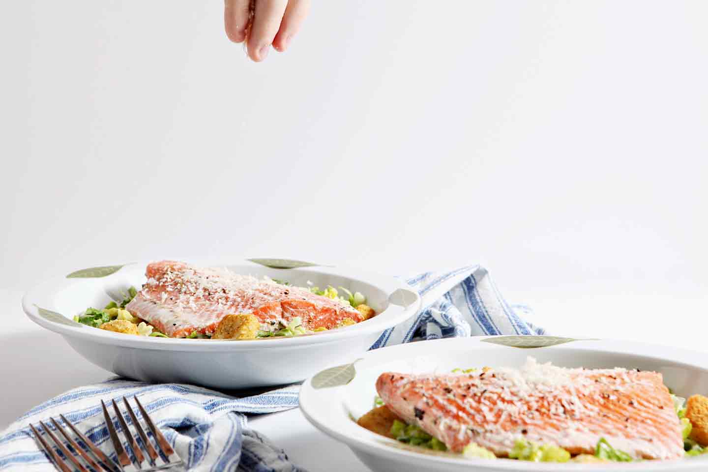 Oven Poached Salmon Caesar Salads being sprinkled with additional parmesan cheese before serving