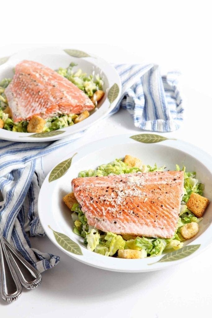 Image of two Oven Poached Salmon Caesar Salads on a white background with a blue-and-white striped towel