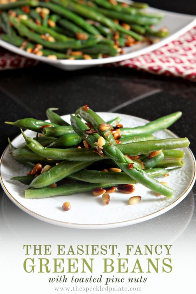 A white plate holds a serving of Vegan Green Beans with Toasted Pine Nuts and shallots with the text 'the easiest, fancy green beans with toasted pine nuts'