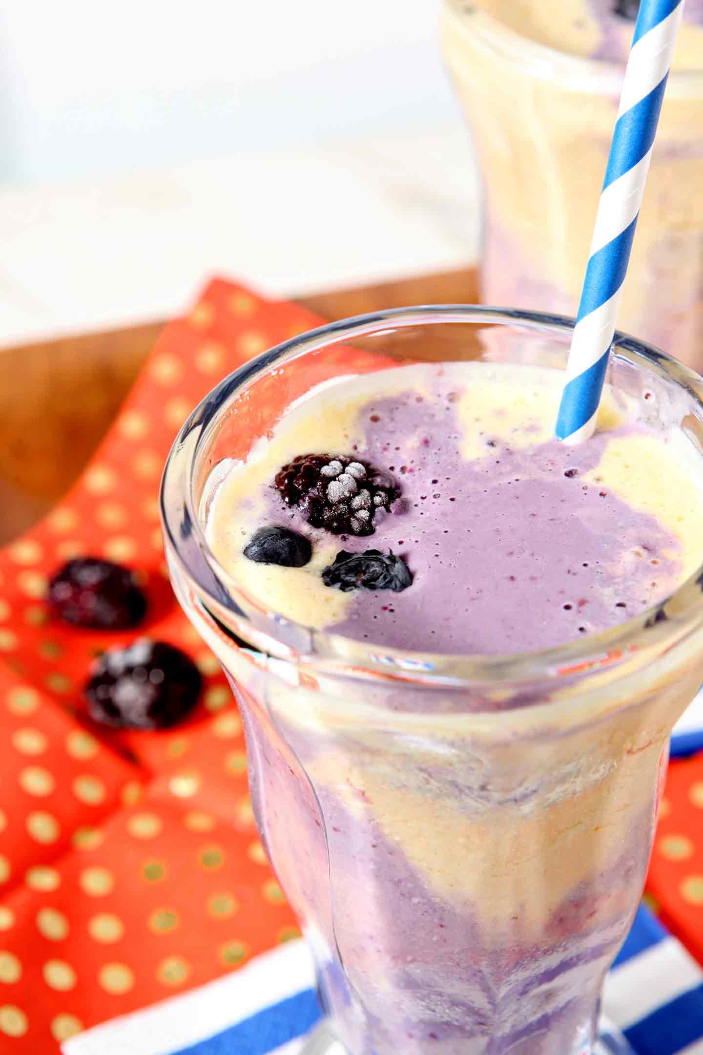 Two Pineapple Blackberry Ice Cream Parfaits are displayed on a wooden tray, covered in an orange napkin, before serving