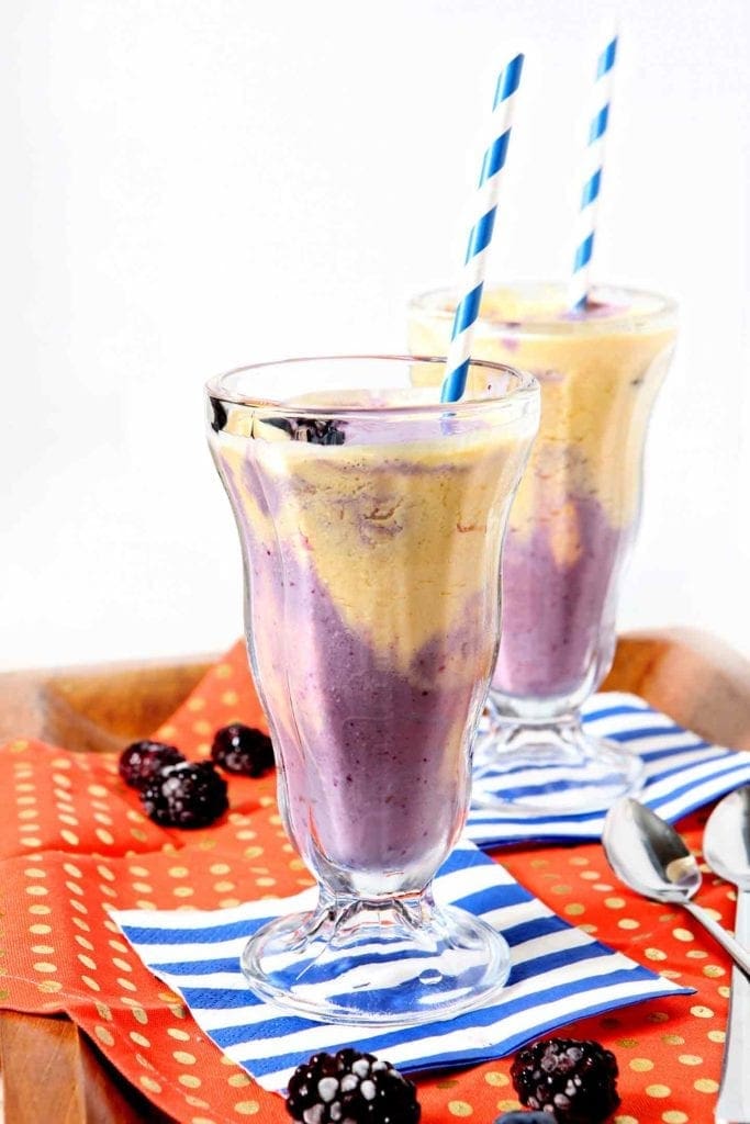 Two Pineapple Blackberry Ice Cream Parfaits are displayed on a wooden tray, covered in an orange napkin, before serving