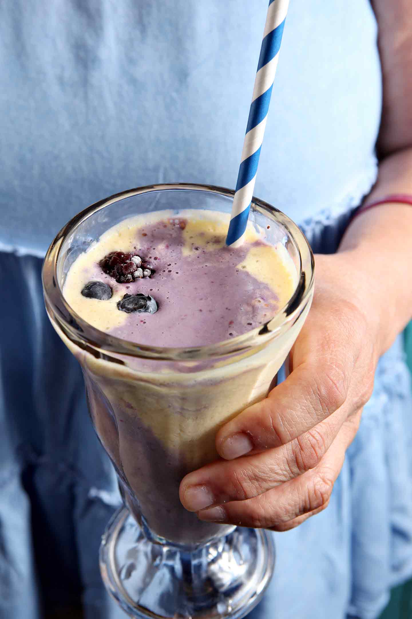 A woman in a blue shirt holds a Pineapple Blackberry Ice Cream Parfait before consuming it