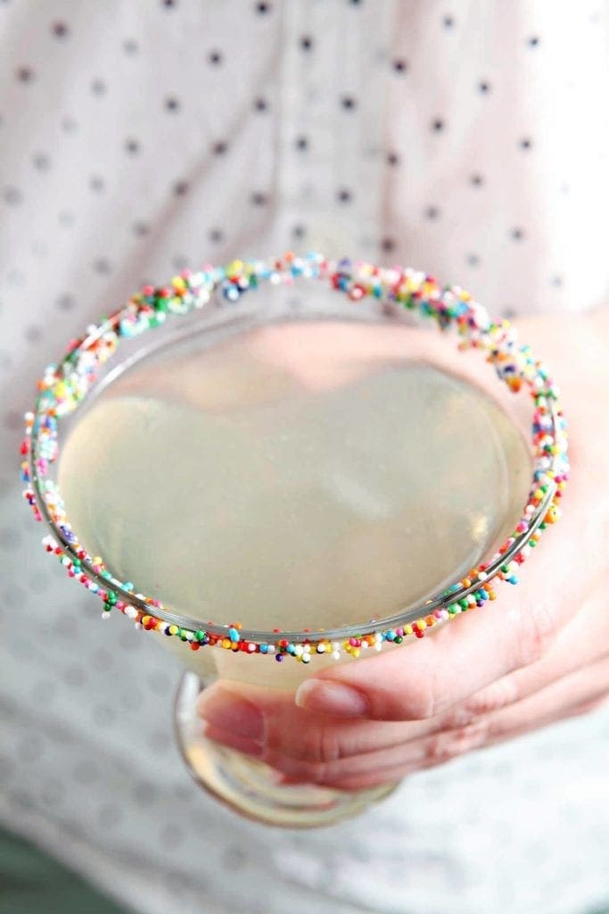 Hand holding a glass of Funfettini Birthday Cake Martini with garnished rim  