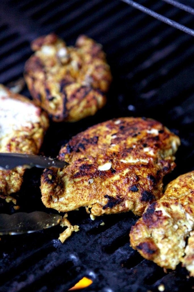 Close up of tongs holding piece of Grilled Chicken Shawarma 