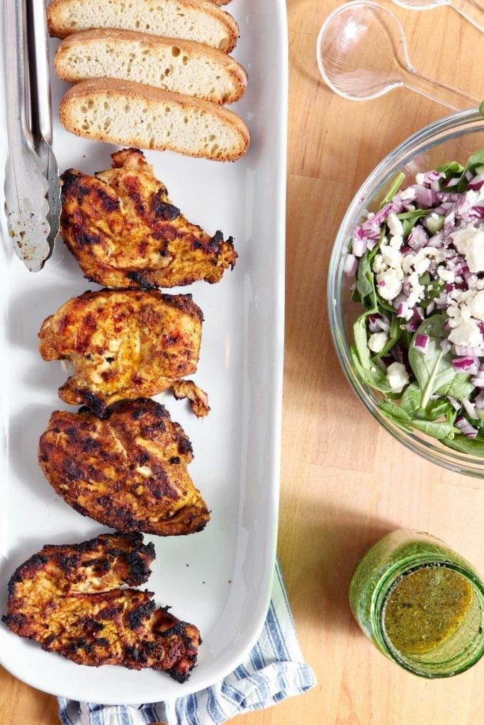 Grilled Chicken Shawarma served on a long white platter with a Greek salad and its dressing displayed beside the platter.