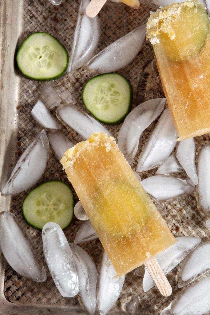 Two popsicles on top of tray with ice and sliced cucumbers 