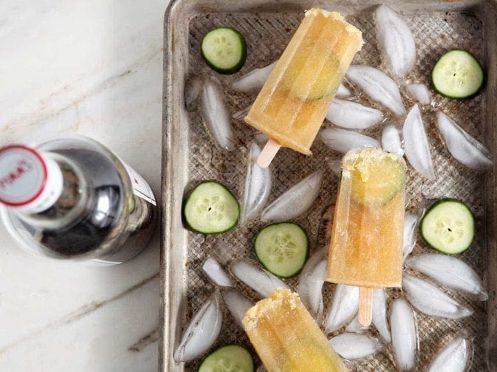 Three popsicles in tray on top of ice and sliced cucumbers