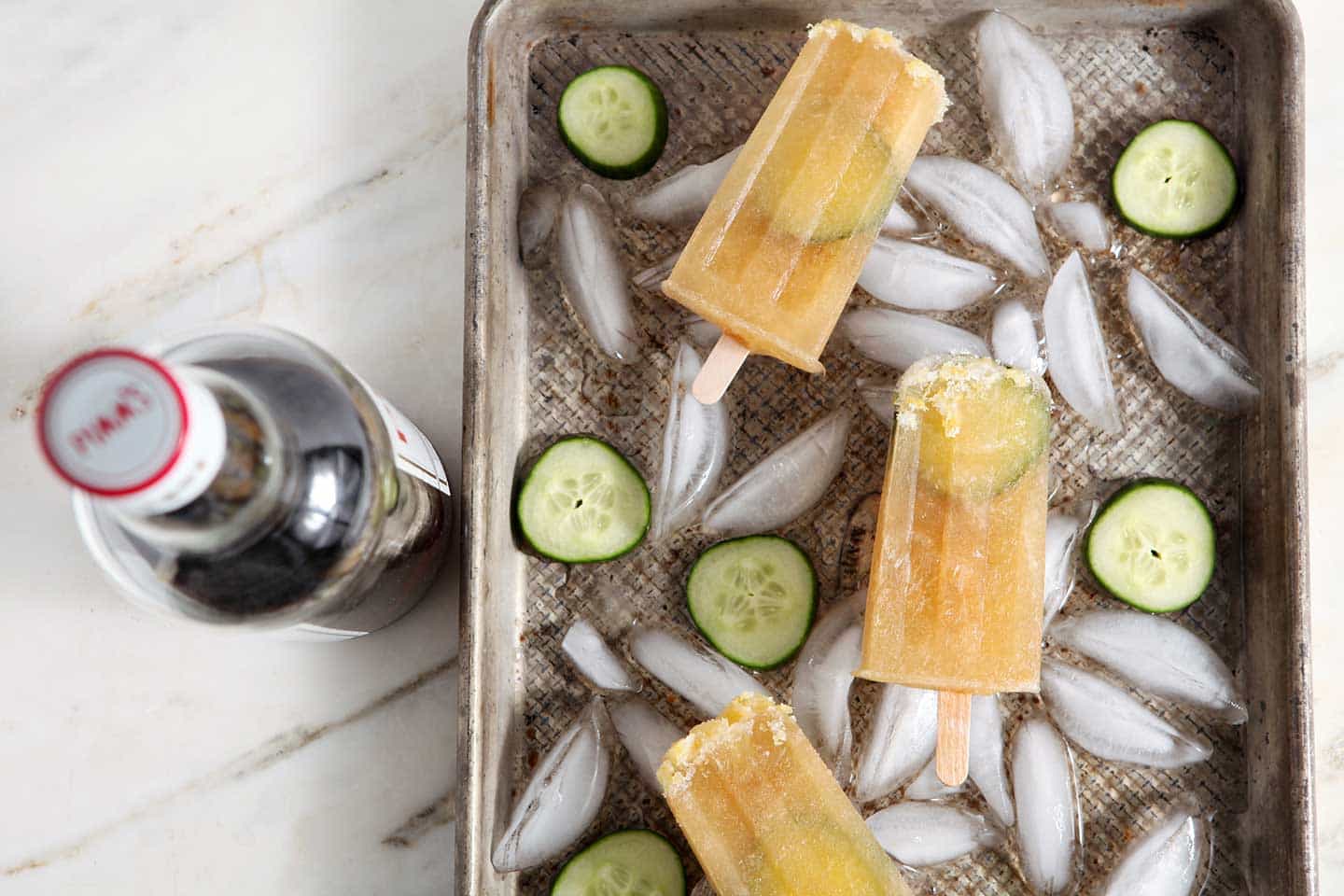 Three popsicles in tray on top of ice and sliced cucumbers