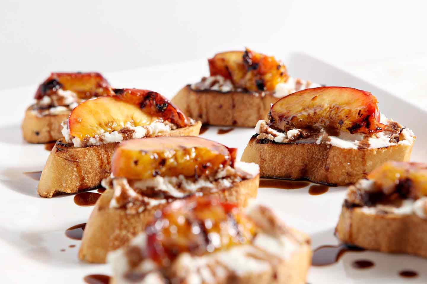 Grilled Peach Bruschetta is a perfect sweet appetizer or dessert for the summertime. Fire up the grill, slice and pit a few fresh peaches, brush the peaches with a little bit of olive oil, then grill until the sugars in the fruit caramelizes. Grill the bread, too. When both are done, smear the bread with fresh ricotta cheese, place the peach slices on top of the cheese, then drizzle with a balsamic vinegar reduction for the final touch. Perfect!