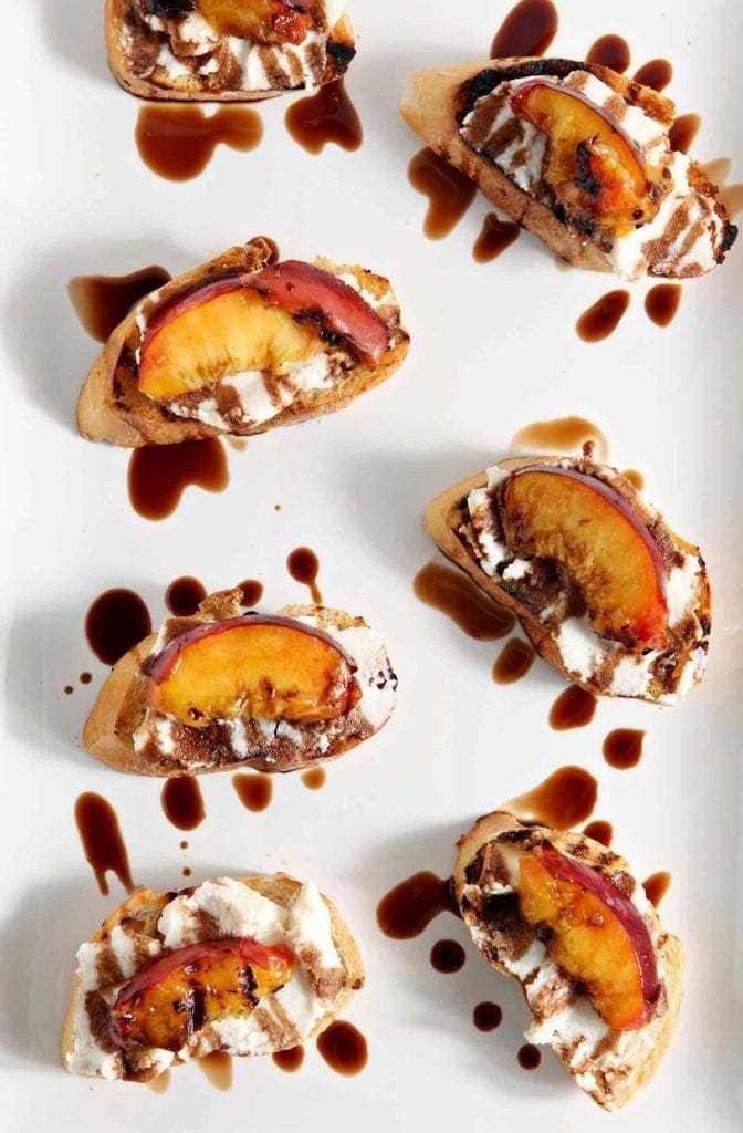 Grilled Peach Bruschetta is a perfect sweet appetizer or dessert for the summertime. Fire up the grill, slice and pit a few fresh peaches, brush the peaches with a little bit of olive oil, then grill until the sugars in the fruit caramelizes. Grill the bread, too. When both are done, smear the bread with fresh ricotta cheese, place the peach slices on top of the cheese, then drizzle with a balsamic vinegar reduction for the final touch. Perfect!