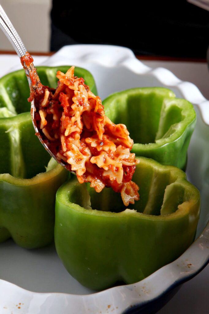 A spoon scoops saucy pasta into bell peppers