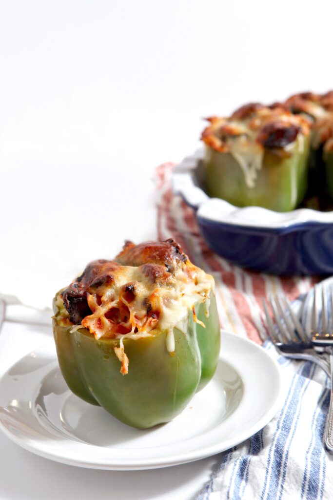 A stuffed bell peppers on a plate covered in cheese in front of a casserole dish with more bell peppers