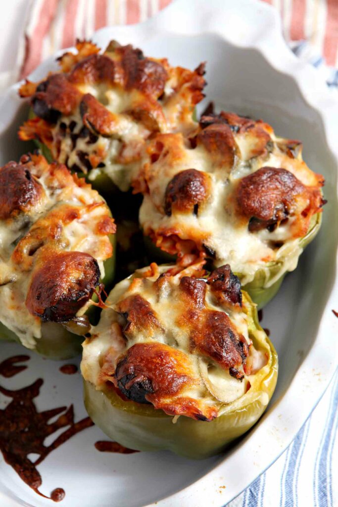 Four cheese-covered baked bell peppers in a casserole dish