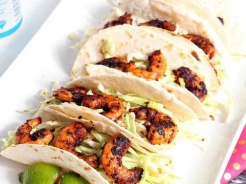 blackened shrimp tacos on a white plate with limes