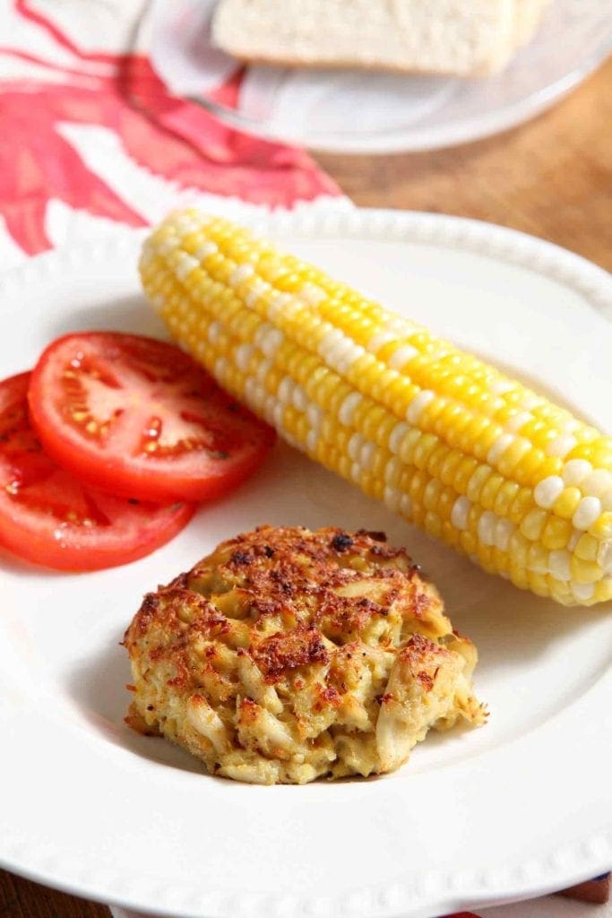 Plate of crab cake, corn on the cob and tomato slices 