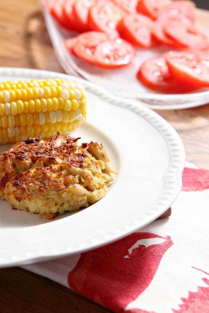 Crab cake on plate with corn on the cob and tomato slices 