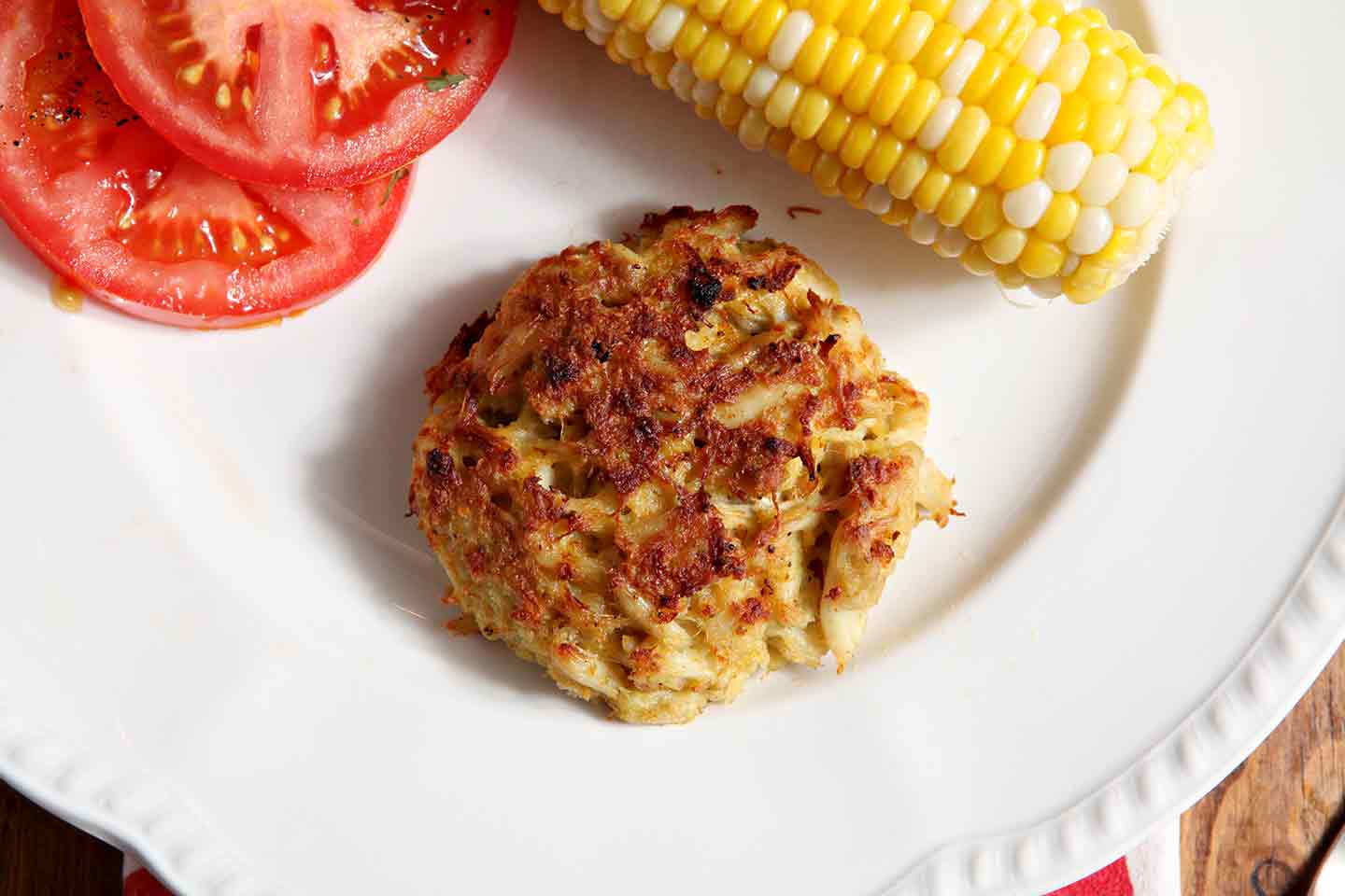 Close up of crab cake, corn on the cob and tomato slices 