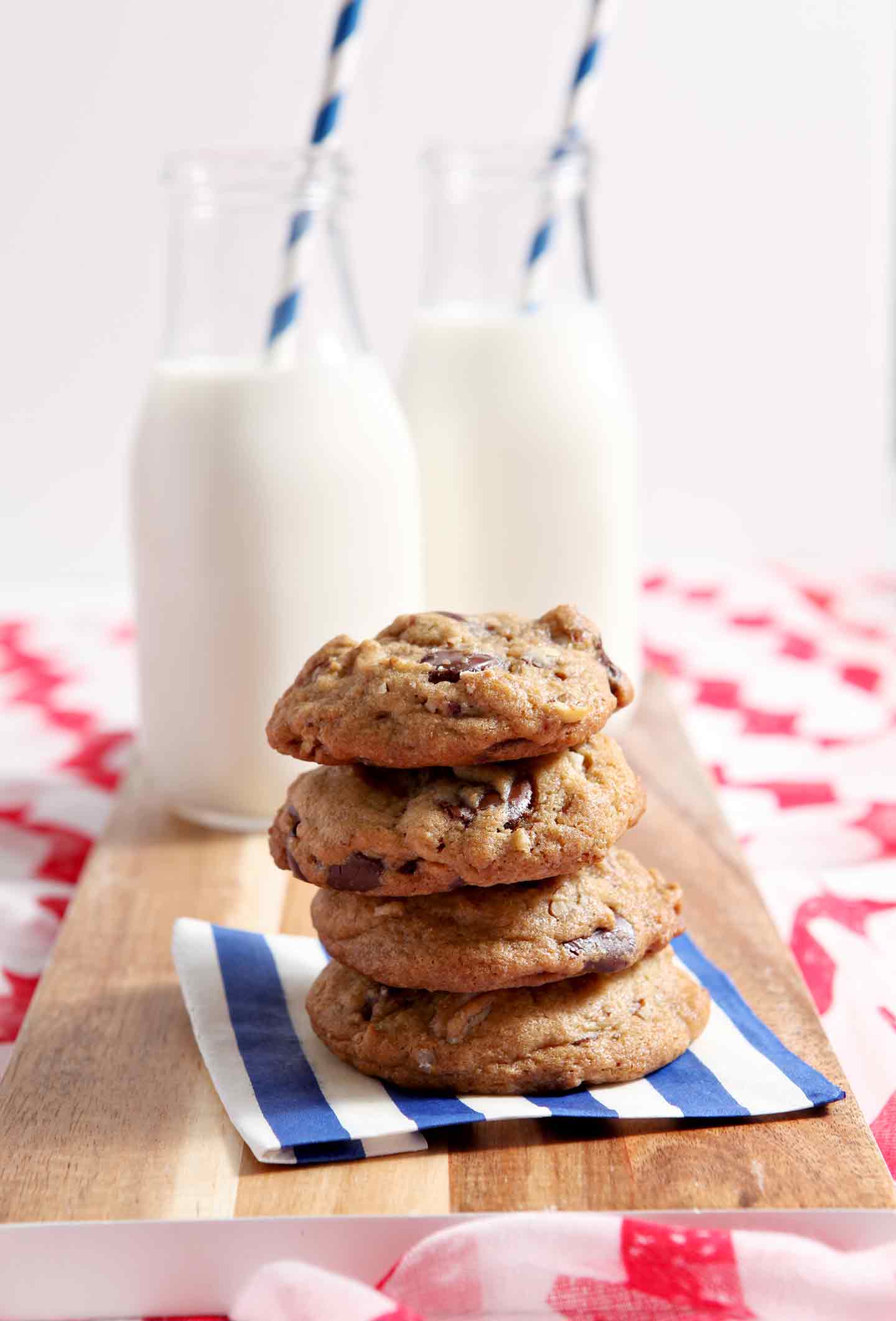 chocolate chip cookies stacked on a blue striped napking with milk