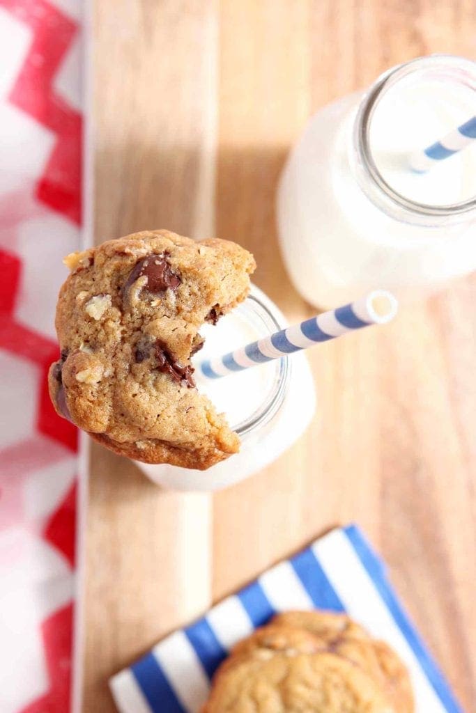 An All-American Chocolate Chip Cookie is perched atop a glass bottle of milk, half-eaten.