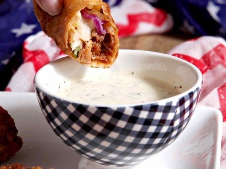 Hand dipping Pulled Pork Coleslaw Eggroll into sauce