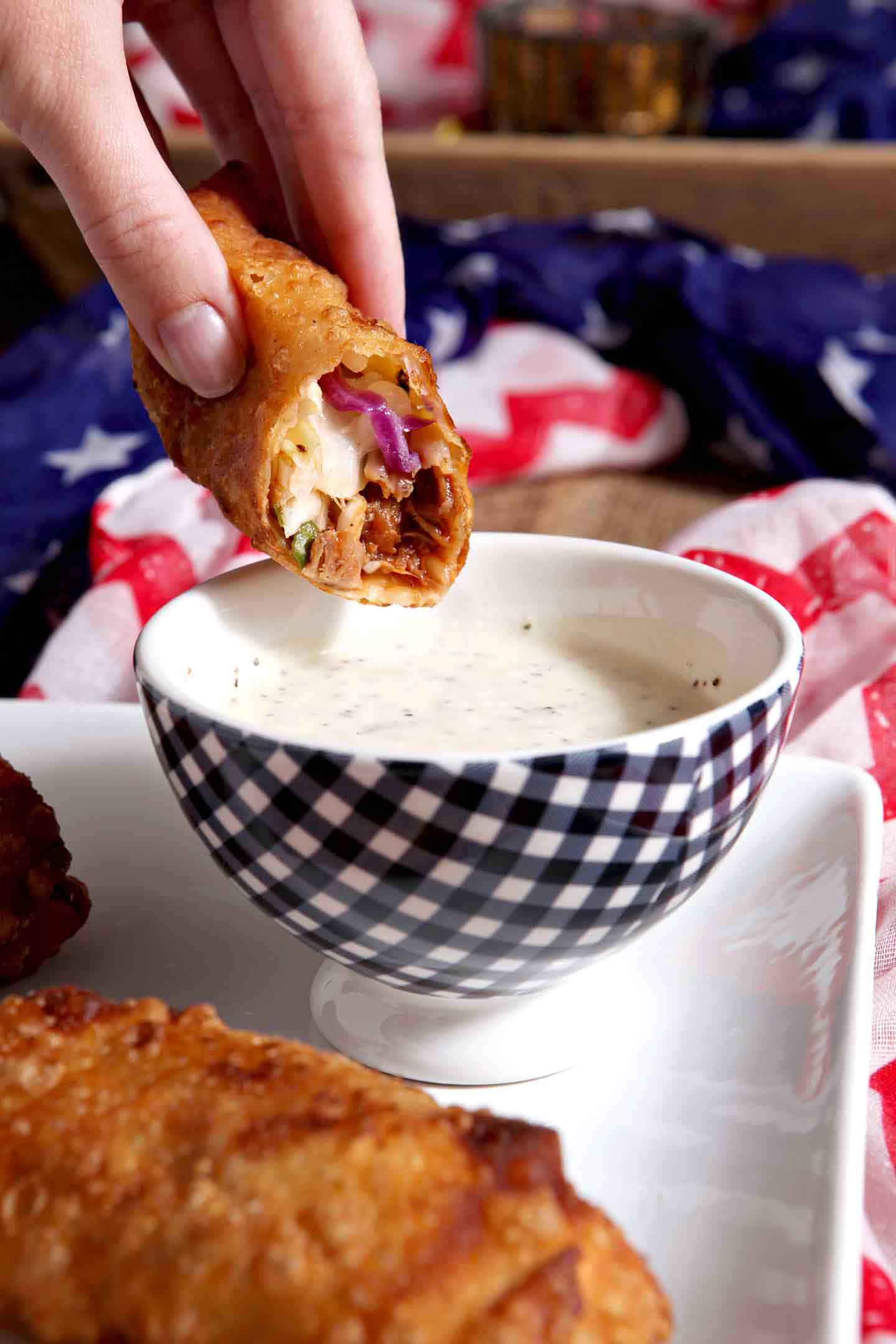 A half-eaten Pulled Pork Coleslaw Eggroll is dipped into the dipping sauce